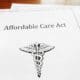 Paperwork on a table top with the first page having the words Affordable Care Act on it and a medical symbol.