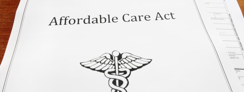 Paperwork on a table top with the first page having the words Affordable Care Act on it and a medical symbol.