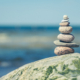 Balancing stones on a big rock with sea grass on the beach, with blue water waves on background, Baltic Sea, Olando Kepure, Lithuania