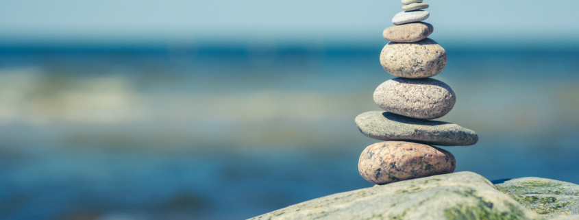 Balancing stones on a big rock with sea grass on the beach, with blue water waves on background, Baltic Sea, Olando Kepure, Lithuania